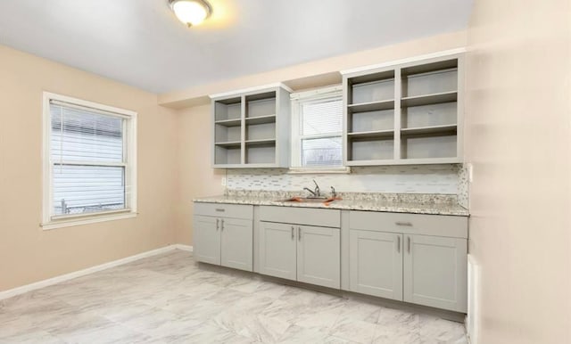 kitchen with tasteful backsplash, gray cabinets, open shelves, a sink, and baseboards