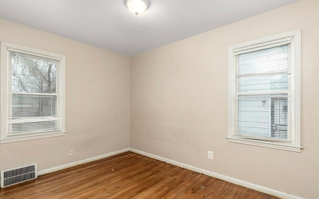 empty room with visible vents, a wealth of natural light, wood finished floors, and baseboards
