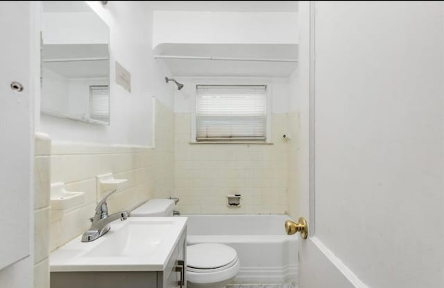 bathroom with a wainscoted wall, toilet, tile walls, vanity, and bathtub / shower combination
