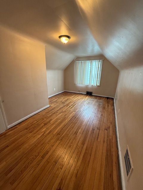 additional living space with hardwood / wood-style floors, baseboards, lofted ceiling, and visible vents