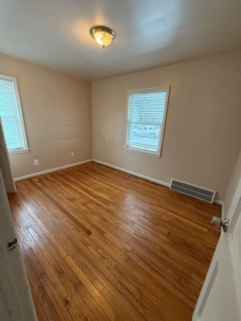 unfurnished room featuring visible vents, a healthy amount of sunlight, baseboards, and wood-type flooring