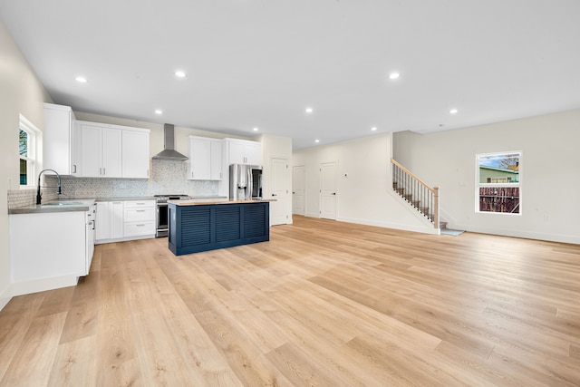 kitchen featuring stainless steel appliances, a sink, wall chimney exhaust hood, a center island, and decorative backsplash