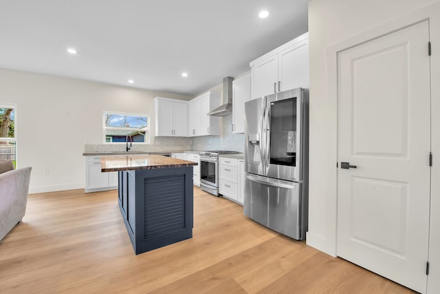 kitchen featuring wall chimney exhaust hood, stainless steel appliances, white cabinets, backsplash, and a kitchen island