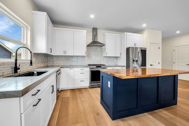 kitchen featuring appliances with stainless steel finishes, wall chimney range hood, wooden counters, a sink, and light wood-type flooring