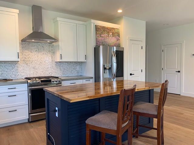 kitchen featuring butcher block counters, wall chimney range hood, light wood-style flooring, and stainless steel appliances
