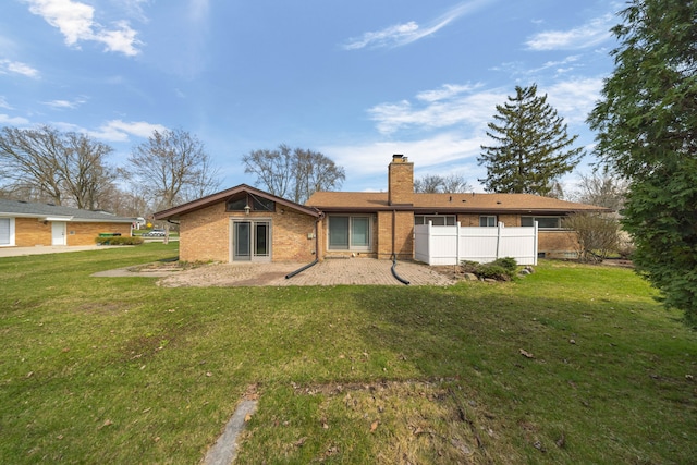 rear view of property featuring a lawn, fence, a chimney, and brick siding