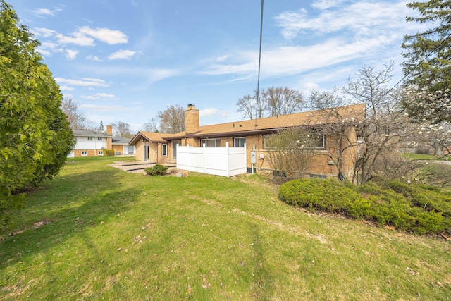back of house featuring a lawn, fence, a chimney, and brick siding