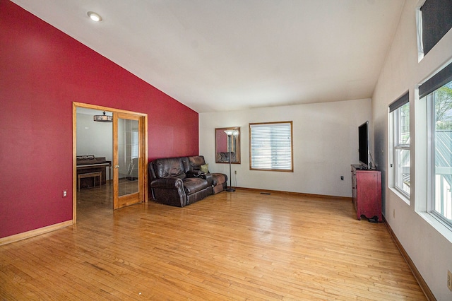 living area with baseboards, light wood finished floors, and lofted ceiling