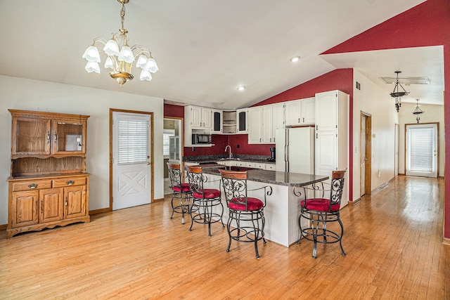 kitchen with a sink, light wood finished floors, freestanding refrigerator, lofted ceiling, and a kitchen bar