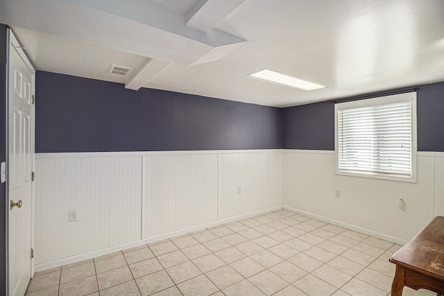 unfurnished room featuring visible vents, light tile patterned floors, and a wainscoted wall