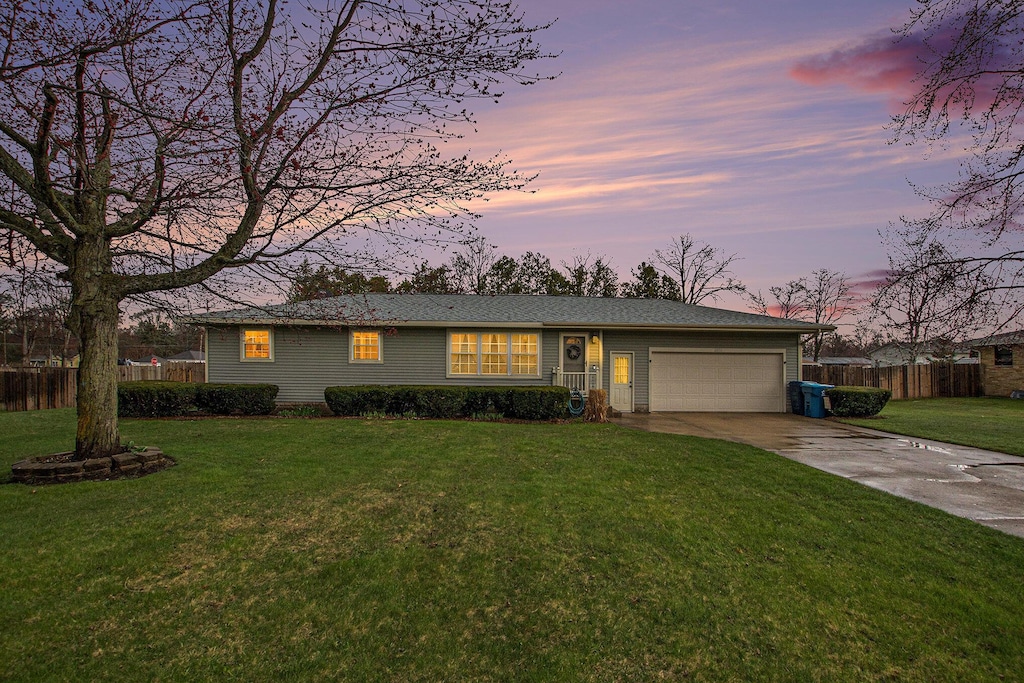 view of front of house with an attached garage, fence, driveway, and a front lawn