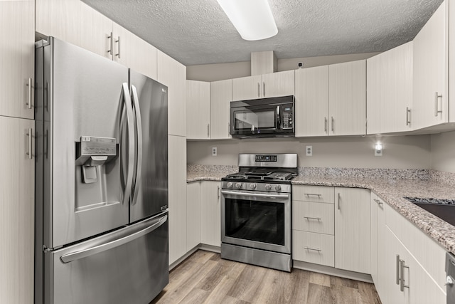 kitchen with light wood finished floors, light stone counters, a textured ceiling, and appliances with stainless steel finishes
