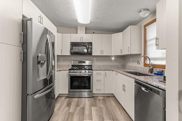 kitchen with light wood-style flooring, stainless steel appliances, a textured ceiling, and a sink