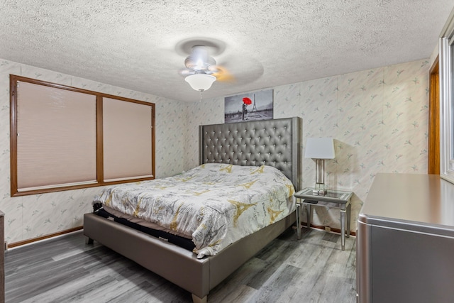 bedroom featuring baseboards, wood finished floors, wallpapered walls, and a textured ceiling