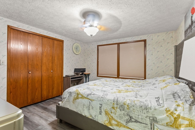 bedroom featuring wallpapered walls, wood finished floors, a textured ceiling, and a closet