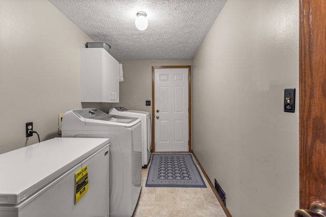 washroom featuring baseboards, cabinet space, washer and clothes dryer, and a textured ceiling