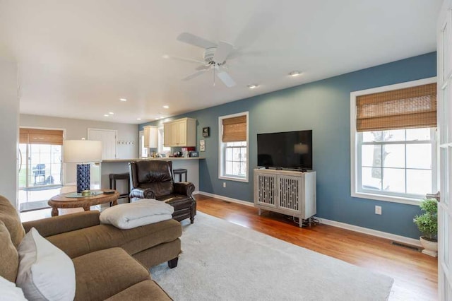 living area featuring light wood-type flooring, plenty of natural light, a ceiling fan, and baseboards