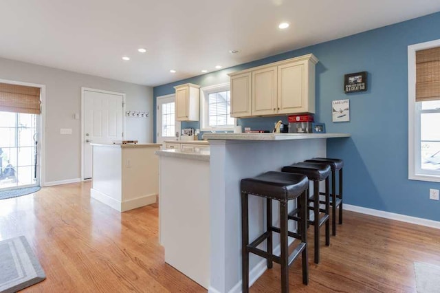 kitchen featuring light wood-style floors, a breakfast bar area, cream cabinets, a peninsula, and a kitchen island