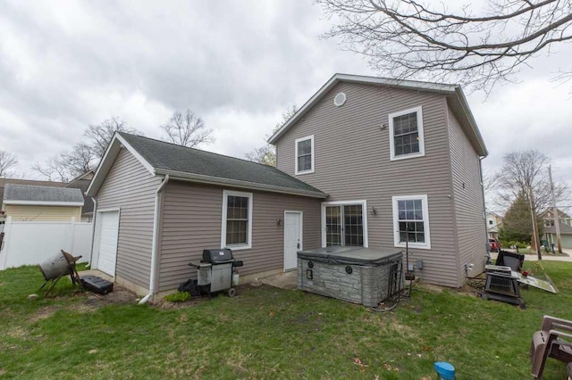back of property with a garage, a yard, a hot tub, and fence