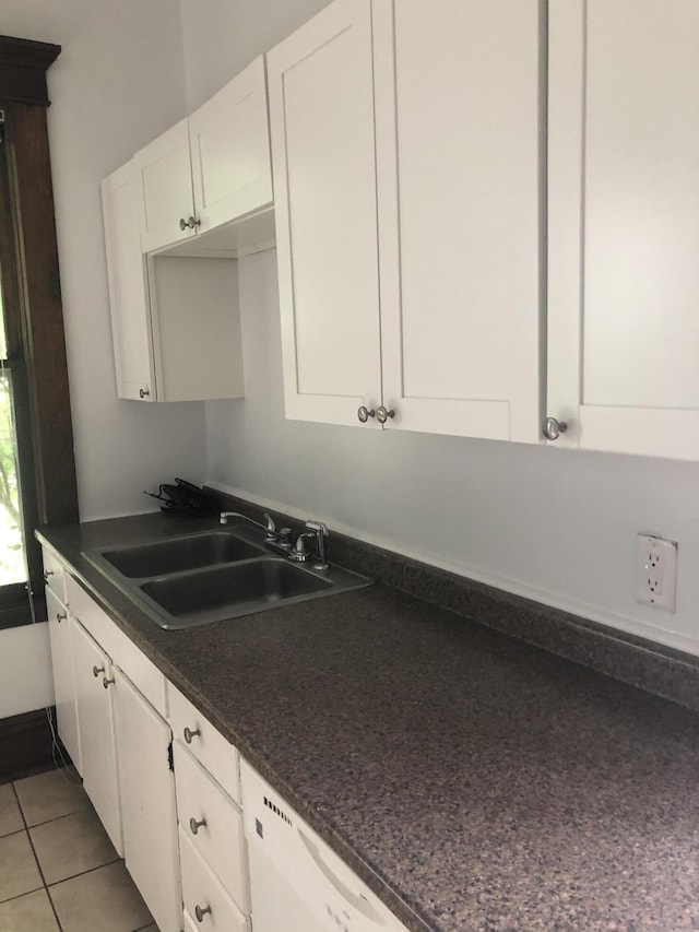kitchen featuring dark countertops, dishwasher, a sink, and white cabinetry