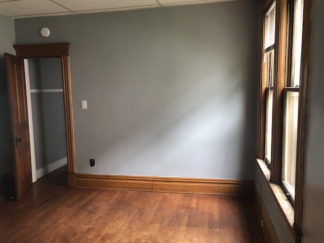 unfurnished room featuring wood finished floors, baseboards, and a drop ceiling