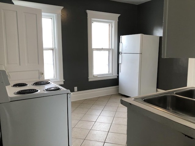 kitchen with baseboards, white appliances, a sink, and light tile patterned flooring