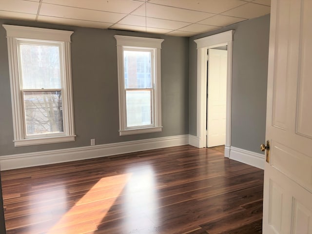 unfurnished room with dark wood finished floors, a drop ceiling, and baseboards