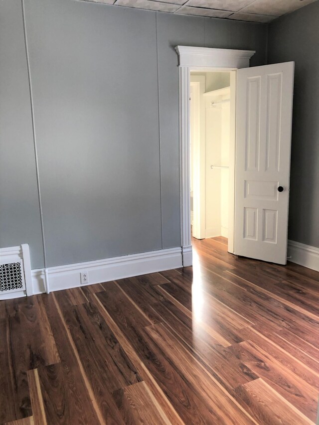empty room featuring dark wood-type flooring, visible vents, and baseboards