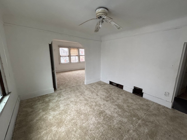 carpeted empty room featuring a baseboard radiator, arched walkways, a ceiling fan, and baseboards