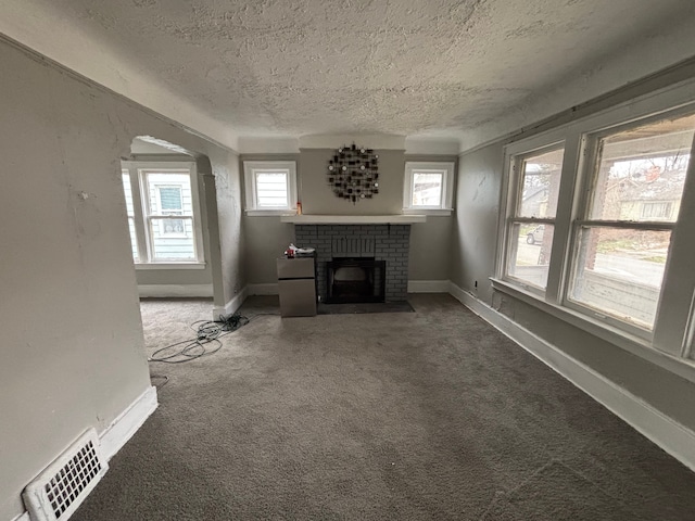 unfurnished living room with a brick fireplace, carpet, a textured ceiling, and visible vents