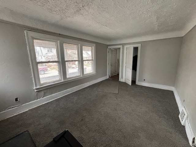 unfurnished bedroom featuring baseboards, dark colored carpet, visible vents, and a textured ceiling