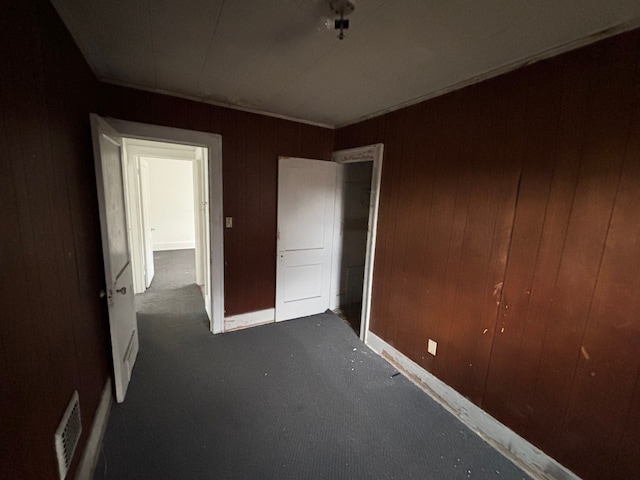 unfurnished bedroom with visible vents, baseboards, wood walls, dark carpet, and a closet