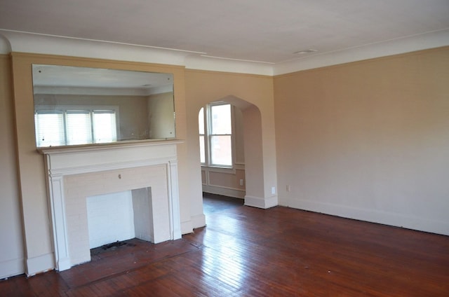 unfurnished living room featuring arched walkways, a healthy amount of sunlight, and dark wood-type flooring