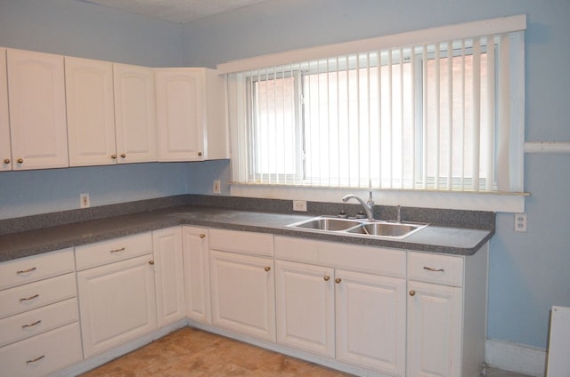 kitchen with a sink, white cabinets, and dark countertops