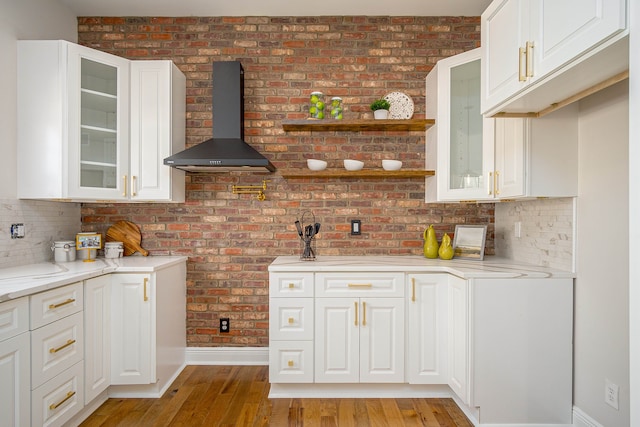 kitchen with wall chimney exhaust hood, baseboards, light wood finished floors, and white cabinetry