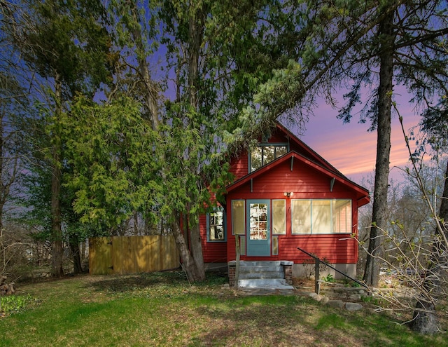 back of house at dusk with fence and a yard