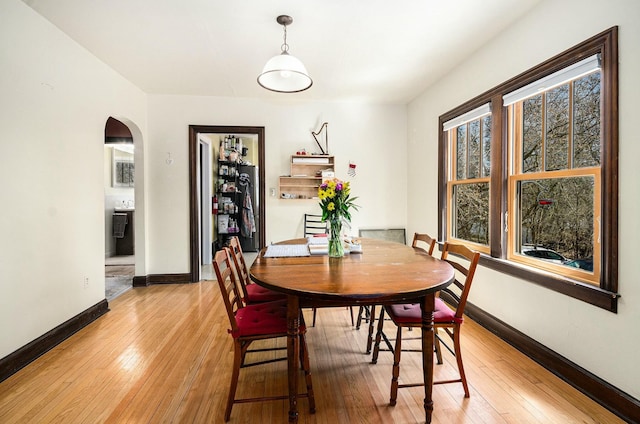 dining space with arched walkways, light wood-type flooring, and baseboards