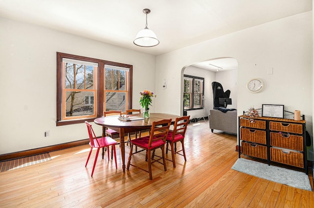 dining space featuring baseboards, arched walkways, light wood-style floors, and plenty of natural light