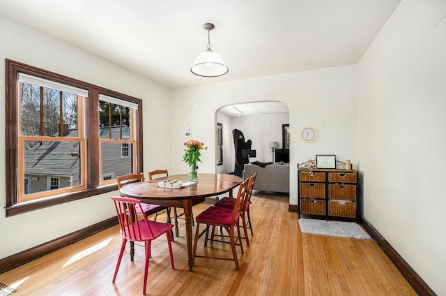 dining area with arched walkways, light wood-style floors, and baseboards