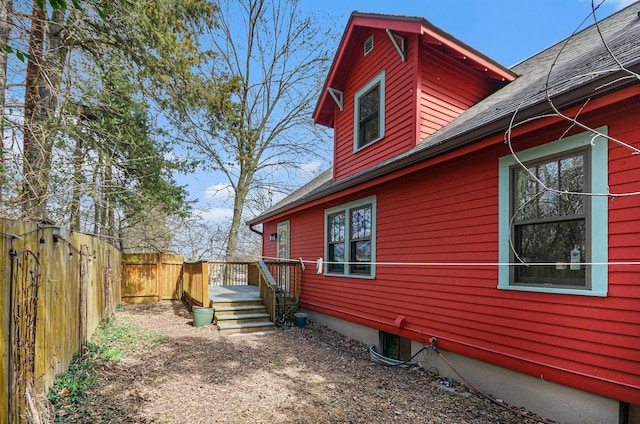 view of side of home featuring fence, a shingled roof, and a deck