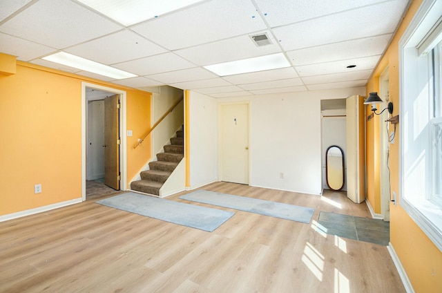 below grade area featuring wood finished floors, visible vents, baseboards, a paneled ceiling, and stairs