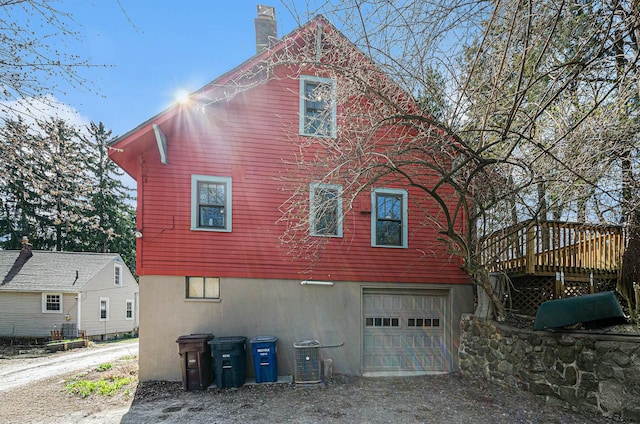 view of side of home featuring driveway, central AC, a chimney, a garage, and a wooden deck