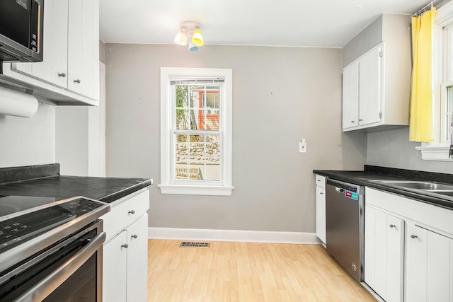 kitchen with light wood finished floors, stainless steel appliances, dark countertops, baseboards, and visible vents