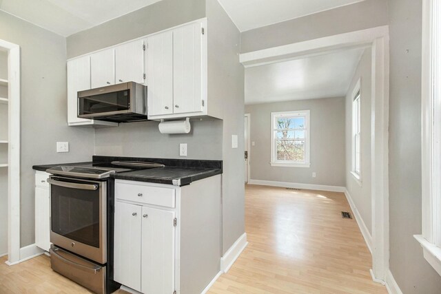 kitchen featuring dark countertops, light wood finished floors, white cabinets, appliances with stainless steel finishes, and visible vents