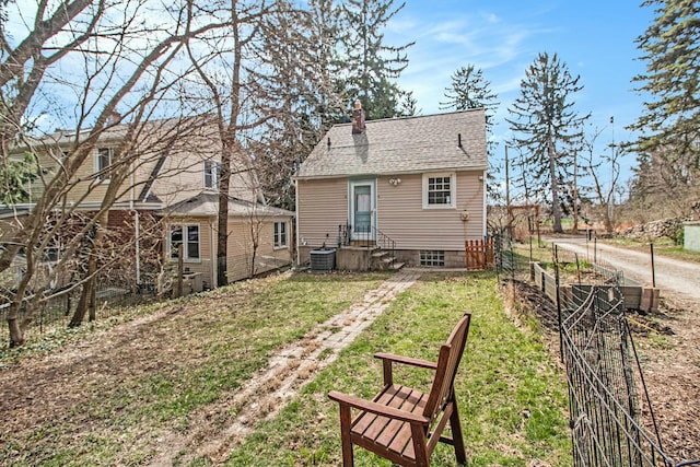 rear view of property featuring cooling unit, a chimney, a lawn, a vegetable garden, and a shingled roof