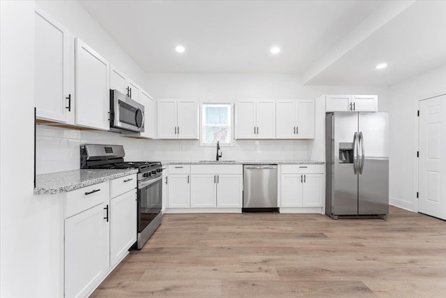kitchen featuring tasteful backsplash, a sink, stainless steel appliances, white cabinetry, and light stone countertops