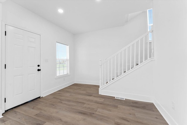 entrance foyer with wood finished floors, visible vents, baseboards, and stairs