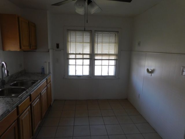 15864 Bringard Dr, Detroit, MI 48205 - kitchen with brown cabinets, a wainscoted wall, light tile patterned floors, a sink, and ceiling fan