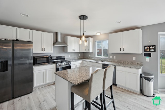 kitchen featuring plenty of natural light, stainless steel appliances, wall chimney range hood, a sink, and light wood-style floors