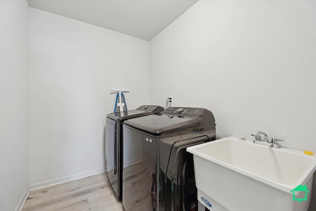 washroom with washing machine and clothes dryer, a sink, light wood-style floors, baseboards, and laundry area